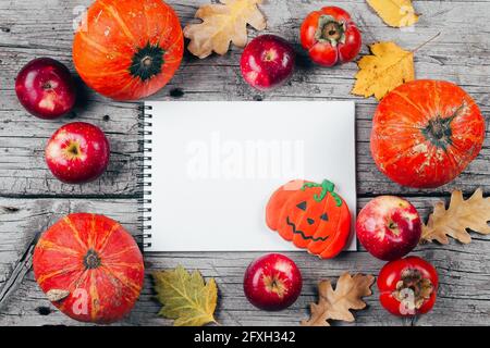 Mockup autunnale. Autunno, concetto di Halloween. Taccuino bianco di carta, biscotti di pan di zenzero, zucche, mele, persimmons e foglie di autunno asciugate su woode Foto Stock