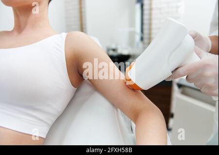 Primo piano di un medico-cosmetologo che esegue la procedura sulla mano del paziente utilizzando apparecchiature mediche laser in un salone di bellezza attrezzato. Professione Foto Stock