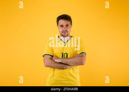 Tifoso brasiliano di calcio in Jersey giallo si pone con le braccia incrociate Foto Stock