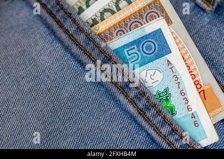 Un sacco di bollette polacche che si stacca dalla tasca posteriore dei pantaloni in denim. Foto scattata in condizioni di luce artificiale e soffusa Foto Stock