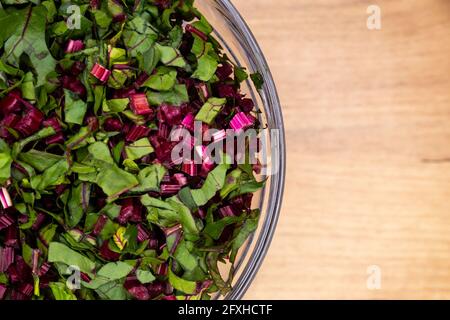 Foglie di barbabietole fresche e tritate disposte in una ciotola di vetro. Foto scattata in condizioni di luce artificiale e soffusa. Foto Stock