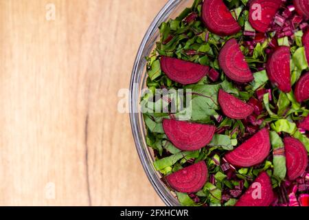 Foglie fresche tagliate e pezzi di barbabietole sistemati in una ciotola di vetro. Foto scattata in condizioni di luce artificiale e soffusa. Foto Stock