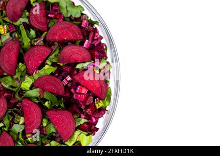 Foglie fresche tagliate e pezzi di barbabietole sistemati in una ciotola di vetro. Foto scattata in condizioni di luce artificiale e soffusa. Oggetto isolato su sfondo bianco Foto Stock