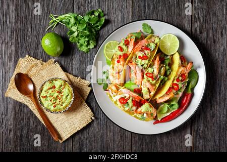 tacos di gamberi grigliati con insalata di cavolo, ripieno di lime e guacamole su un piatto su un tavolo di legno, piatto Foto Stock