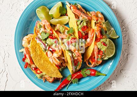 conchiglie di taco con gamberi alla griglia, insalata di cavolo, lime e guacamole su un piatto blu su un tavolo bianco, piatto, spazio libero, primo piano Foto Stock