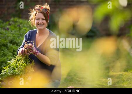 Ritratto felice donna sicura raccogliendo patate fresche in giardino Foto Stock