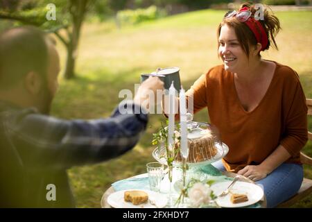 Buona coppia gustando il tè e la torta al tavolo in un giardino soleggiato Foto Stock