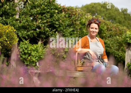 Ritratto donna felice che prende una pausa dal giardinaggio in giardino soleggiato Foto Stock