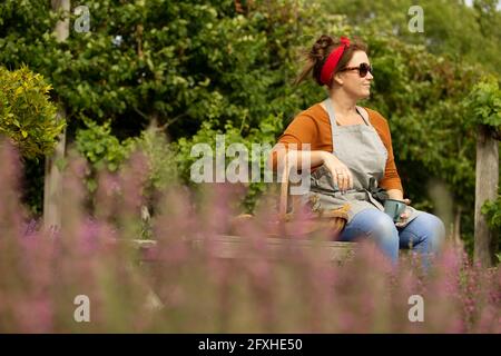 Donna in occhiali da sole che prende una pausa dal giardinaggio nel cortile estivo Foto Stock