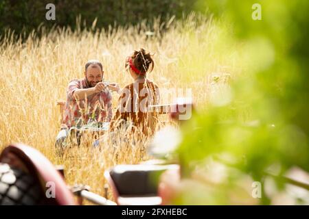 Accoppia i bicchieri d'acqua per tostare in un'erba alta e soleggiata dietro il trattore Foto Stock