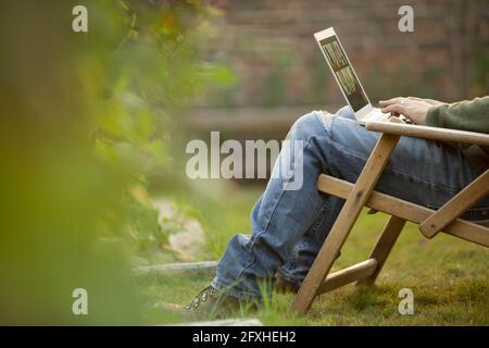 Uomo che usa un computer portatile in sedia da prato in giardino Foto Stock