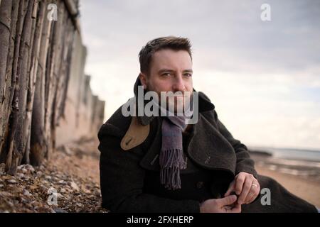 Ritratto uomo bello sicuro in cappotto invernale sulla spiaggia Foto Stock
