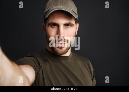 L'uomo militare è soddisfatto di scattare foto selfie e guardare la fotocamera isolato su sfondo nero Foto Stock