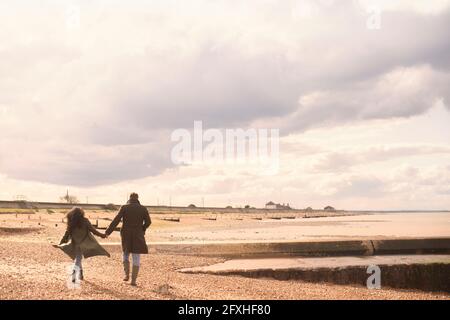 Coppia che tiene le mani camminando sulla soleggiata e tranquilla spiaggia invernale Foto Stock