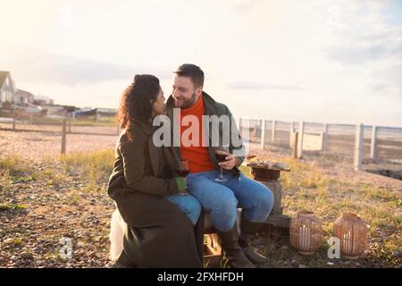 Felice coppia romantica gustando vino dal fuoco sul patio invernale della spiaggia Foto Stock