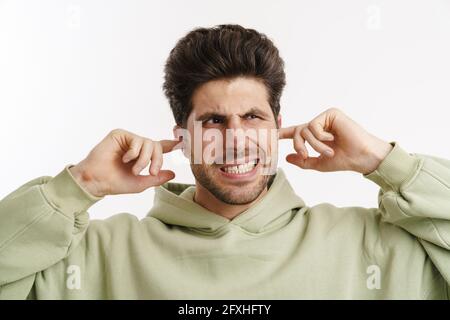 Infastidito uomo bello in sportswear tappando le orecchie isolate sopra sfondo bianco Foto Stock