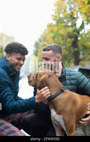 Felice coppia gay maschio che accarezzano il cane sulla strada Foto Stock