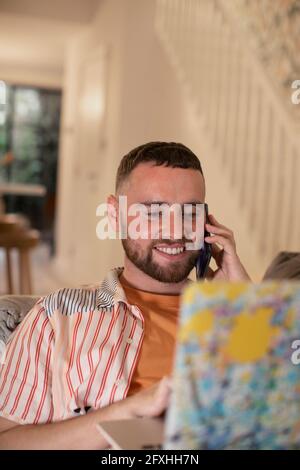 Un giovane sorridente che parla con uno smartphone al computer portatile Foto Stock