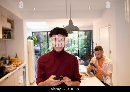 Ritratto giovane felice sicuro usando lo smartphone in cucina Foto Stock