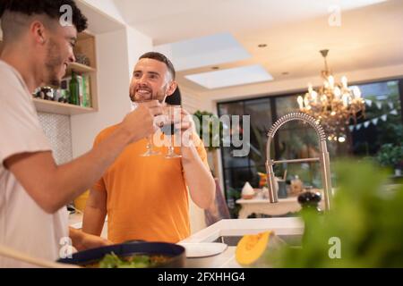 Felice coppia gay maschio bere vino e cucinare in cucina Foto Stock