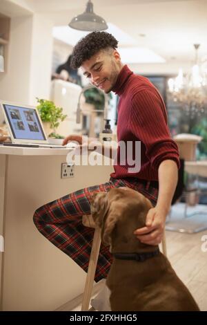 Giovane uomo che lavora da casa al computer portatile e cane in cucina Foto Stock