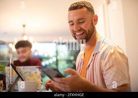 Felice giovane uomo utilizzando smart phone a casa Foto Stock