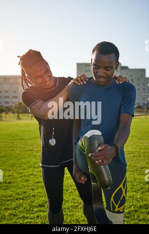 Allenatore che sostiene un giovane atleta maschile amputato che si estende nel parco Foto Stock