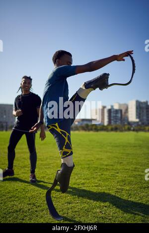 Allenati guardando un giovane atleta maschile amputato che si allunga nel parco soleggiato Foto Stock