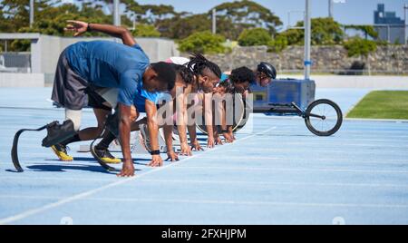 Diversi atleti pronti alla partenza sulla soleggiata pista sportiva blu Foto Stock