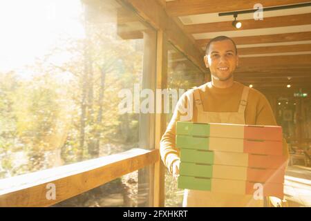 Ritratto orgoglioso proprietario di pizzeria maschile con scatole di pizza alla finestra soleggiata Foto Stock