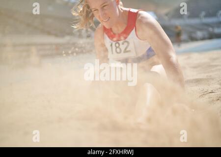 Atleta da campo e pista che atterra in sabbia a salto lungo Foto Stock