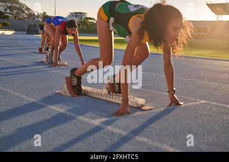 Atlete da campo e da pista a blocchi di partenza su pista soleggiata Foto Stock