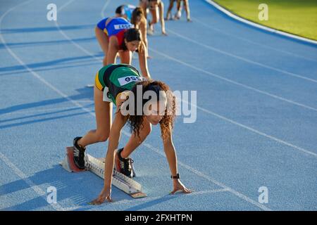 Atlete da campo e da pista pronte a blocchi di partenza su pista blu Foto Stock