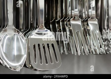 Foto di acciaio inossidabile vari utensili da cucina appesi al rack del negozio. Foto Stock