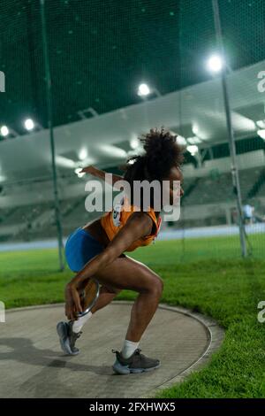 Pista femminile e atleta da campo che getta discus nello stadio di notte Foto Stock