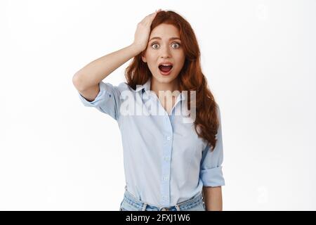 Immagine di donna rossa sorpresa ricordare qualcosa, lanciando un'idea, tenendo la mano sulla testa e fissando in stupore alla macchina fotografica, caduta mascella, in piedi in blusa Foto Stock