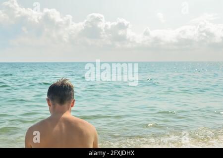 Solitario giovane uomo sulla spiaggia estiva su calmo sfondo di mare. Foto Stock