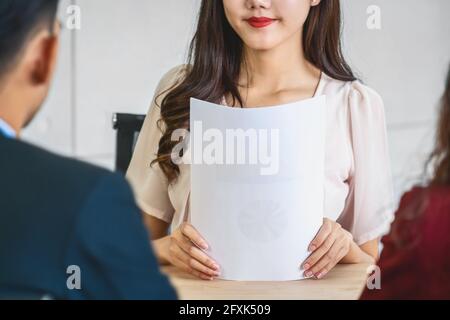 Closeup giovane donna asiatica laureata tenendo il documento del resume e. preparazione a due manager prima di iniziare il colloquio di lavoro con movimento positivo in meet Foto Stock