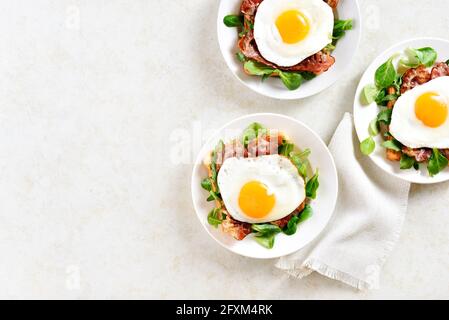 Aprire i sandwich con uova fritte, pancetta e foglie di verdure sul piatto su uno sfondo di pietra chiaro con spazio libero per il testo. Vista dall'alto, disposizione piatta Foto Stock