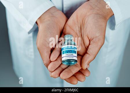 closeup di un operatore sanitario, indossando un camice da laboratorio bianco, con una bottiglia vaccino covid-19 simulata nelle sue mani Foto Stock