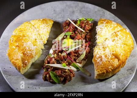 Tartare di bistecca servito con pane alla Foccacia di stile italiano. Il piatto è fatto con manzo crudo, tuorlo d'uovo e altri ingredienti freschi. Foto Stock