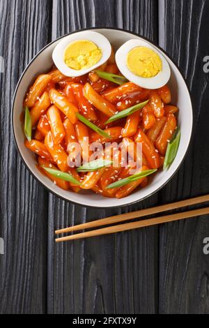 Tteokbokki è uno dei cibi di strada coreani più popolari in Corea primo piano in una ciotola sul tavolo. Vista dall'alto verticale Foto Stock