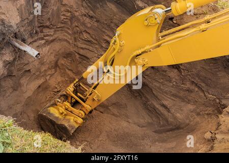 Il pistone idraulico della benna dell'escavatore con il terreno scava un foro nella parte più vicina del cantiere. Foto Stock