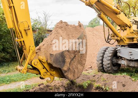 Un secchio di escavatore con un mucchio di sabbia e un fondo terreno. Lavori industriali sul cantiere. Foto Stock