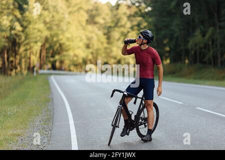 Giovane seduto in bicicletta e bevendo acqua dolce Foto Stock