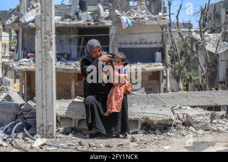 Gaza. 27 maggio 2021. La madre del bambino palestinese, Imad Naseer, bagna il suo bambino in un contenitore di plastica sulle macerie della sua casa distrutta a Beit Hanoun. I residenti di Beit Hanoun soffrono della mancanza di acqua ed elettricità nella zona a causa della grande distruzione che ha colpito la zona a causa dei bombardamenti israeliani nella striscia di Gaza settentrionale. Credit: Notizie dal vivo di Mmaggioranza del mondo CIC/Alamy Foto Stock