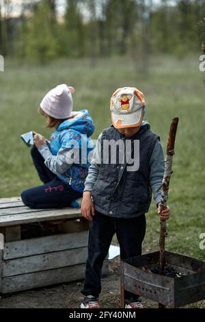 Kiev, Ucraina - Maggio, 15: La bambina gioca app sul suo cellulare fuori. Il ragazzino vicino a lei gioca con bastone. Due bambini si annoiano giocando l'uno con l'altro. Concetto di gioco moderno per bambini. Copia Foto Stock