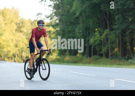 Giovane uomo in bicicletta su strada tra la foresta verde Foto Stock