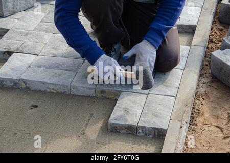 Costruzione di pavimentazione vicino alla casa. Lo strato di mattoni posiziona blocchi di pietra per pavimentazione in calcestruzzo per la costruzione di un marciapiede Foto Stock