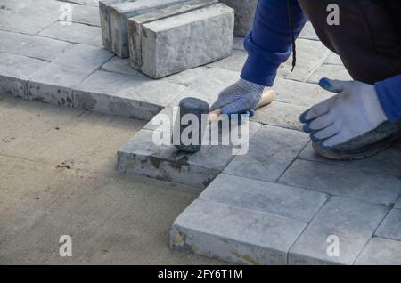 Costruzione di pavimentazione vicino alla casa. Lo strato di mattoni posiziona blocchi di pietra per pavimentazione in calcestruzzo per la costruzione di un marciapiede Foto Stock